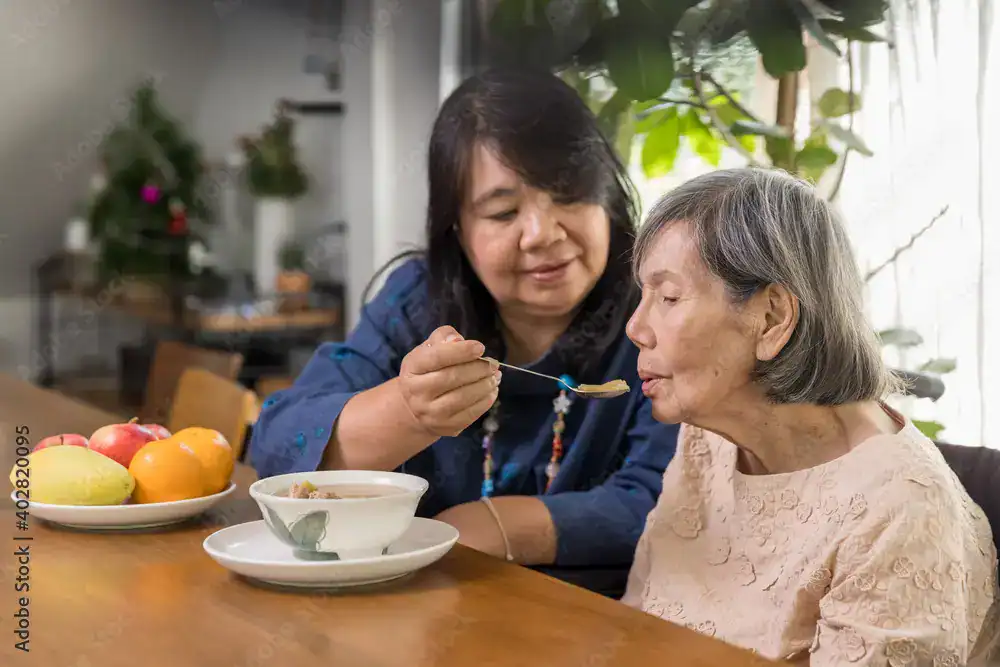 Trusted In-Home Senior Care – Austin, Tx for aged - caregiver lovingly feeding elderly client fresh fruit and soup at the dining table in a cozy home setting